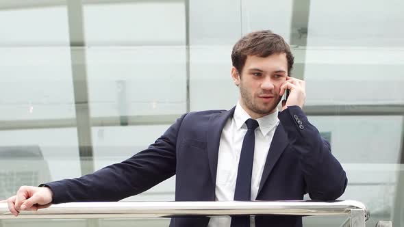 Young Confident Businessman Is Corporate Negotiating at Smartphone in Lobby of Modern Office