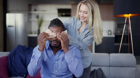 Caucasian Woman Closing Eyes of African American Man with Hands Smiling