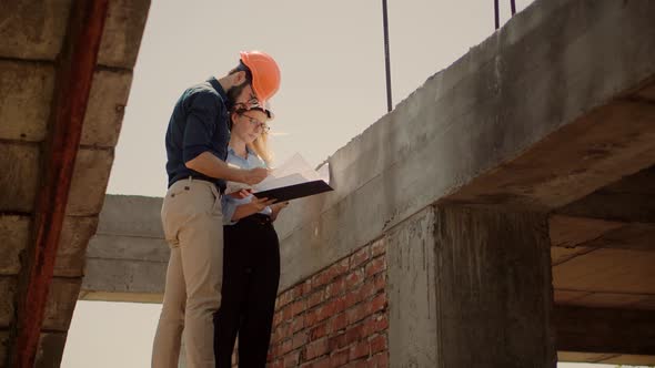 Two Architects Working On Building Model Blueprints. Engineers In Safety Helmet Construction House.