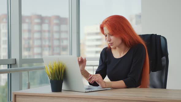 Young Attractive Woman of Caucasian Appearance and Red Hair Working in the Office on a Laptop. The