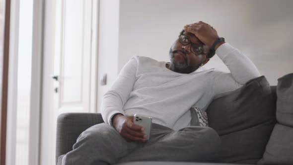 Cheerful African man looking at phone on the sofa