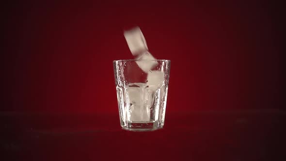 Slow Motion Ice Cubes Falling in Transparent Glass on Red Background. A Mug Stands on a Mirrored