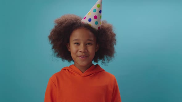 Smiling African American girl in birthday party hat talking to camera