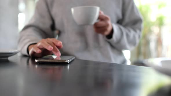 Closeup of a woman touching and scrolling on smart phone screen while drinking coffee