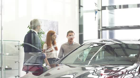 Couple Talking with Mature Sales Manager While Choosing a Car in Dealership