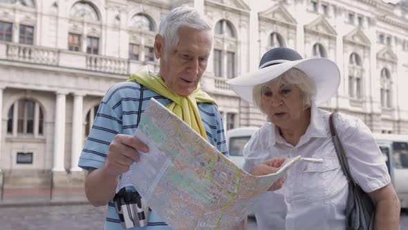 Senior Male Tourist Asking Woman for Directions in Town Using a Map in Hands