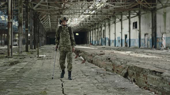Female Soldier Walking with Crutch Through Destroyed Factory
