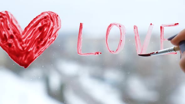 Female Hand Draws Red Heart Word LOVE on the Window with Paint