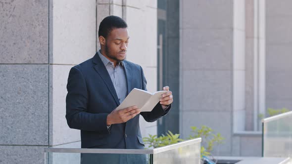 Serious Confident Black Man Wearing Suit Holding Day Planner Reading Paper Book or Business Notebook