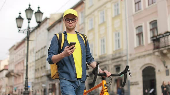 A Young Delivery Man is Going and Texting on a Smartphone