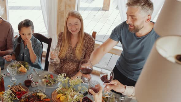 Man Giving Toast and Clinking Glasses with Family Members at Holiday Dinner