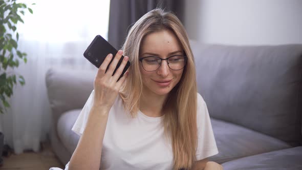 Blonde Girl Using Virtual Assistant on Mobile Phone Listening Audio Message and Smiling