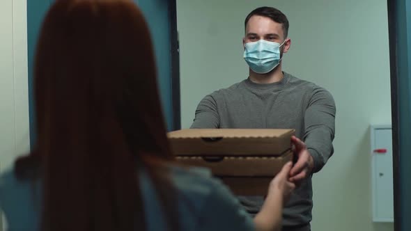 Handsome Delivery Man Wearing Medical Face Mask Delivering Boxes with Hot Pizza To Redhead Customer