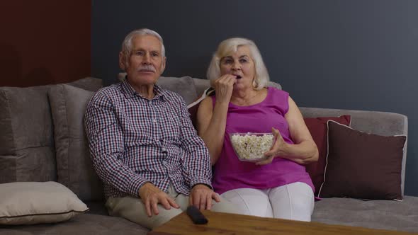 Senior Couple Is Enjoying Watching a Movie on TV and Eating a Popcorn on Sofa in Living Room at Home