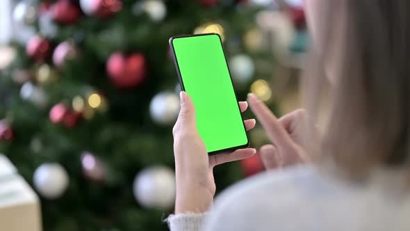 Woman Using Green Mock-up Screen Smartphone Near Christmas Decoration