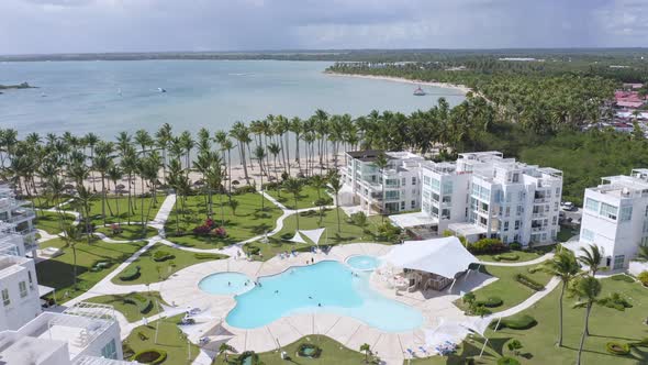 Aerial backwards shot of luxury Hotel resort with pool, private beach between palm trees and Caribbe