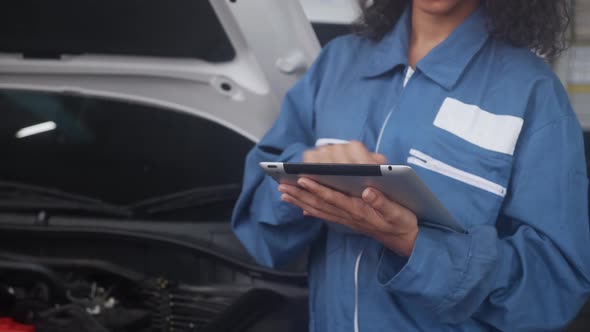 Young woman is mechanic holding tablet computer checking engine of car in the garage.