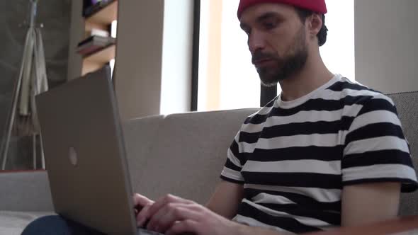 Guy - freelancer sitting on the couch, working on a laptop.