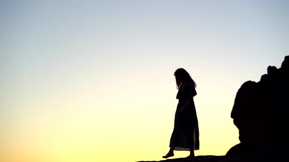 Female silhouette walking on rocky hilltop at picturesque sunset