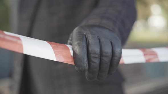 Close-up of Male Hand in Leather Glove Touching Red and White Tape Barrier Outdoors. Unrecognizable