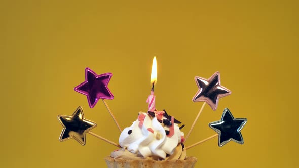 Birthday Cupcake with Candles and Birthday Decorations on Yellow Background