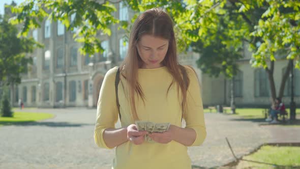 Young Redhead Woman Counting Money, Putting Dollars in Back Pocket and Crossing Hands. Portrait of