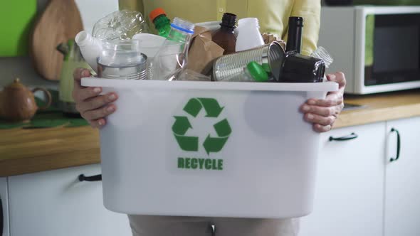 Responsible Woman is Showing Basket with Waste for Recycling Standing in Kitchen Interior