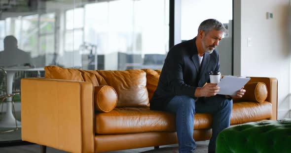 Businessman with coffee cup checking document on sofa 4k