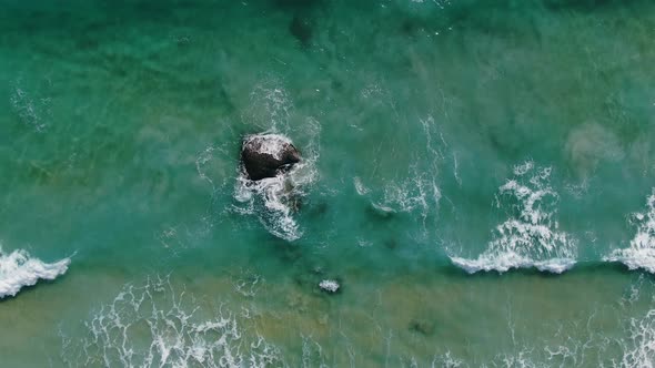 Top view of ocean waves crashing against an empty stone white foaming surf to clean water.