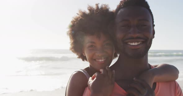 Portrait of smiling african american couple embracing on sunny beach