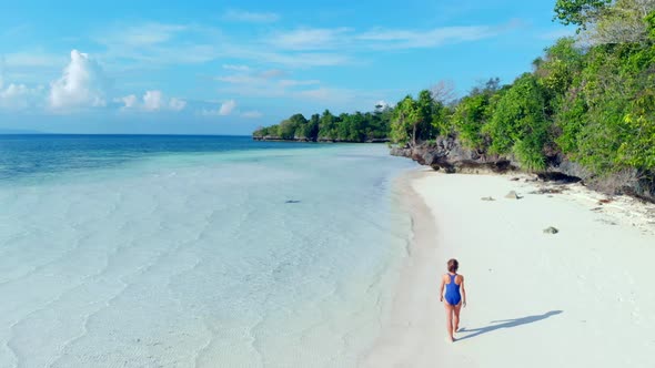 Aerial: woman walking on desert beach, tropical island white sand beach turquoise caribbean sea