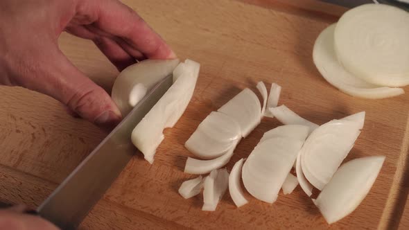 Chef slices fresh white onions on a wooden cutting board