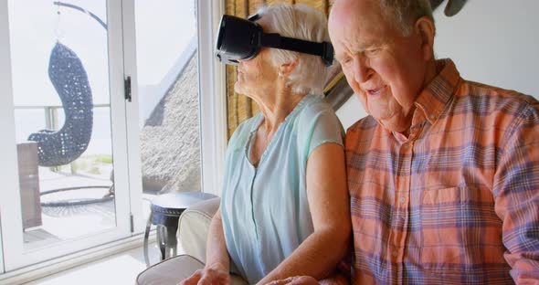 Front view of Caucasian senior woman using virtual reality headset and senior man siting on sofa at