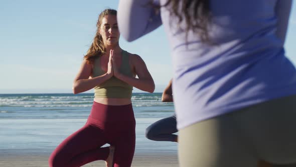 Group of diverse female friends practicing yoga at the beach