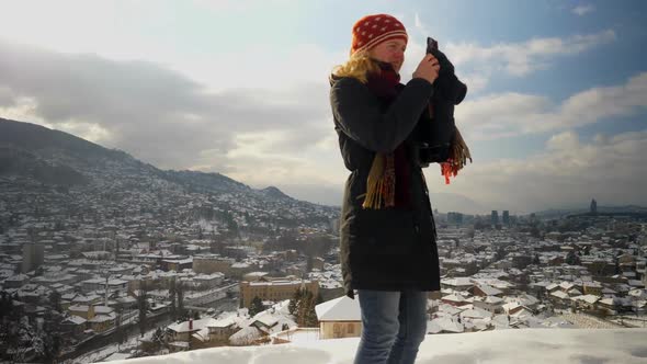 Medium shot of woman standing on a hill in Sarajevo and turning while taking a video with her phone