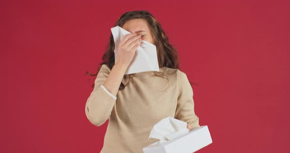 Caucasian Young Adult Girl Sick Woman Millennial Teenager Stands in Studio on Red Background Sneezes