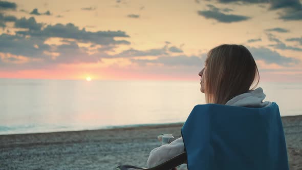 Young Woman Drinking From Thermos and Sitting on Camping Chairs on the Beach