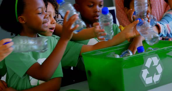 Schoolkids putting bottles in recycle container at desk in classroom 4k