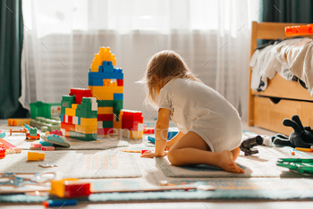 Baby girl playing indoors sitting on floor in playroom at home with constructor. Educational game