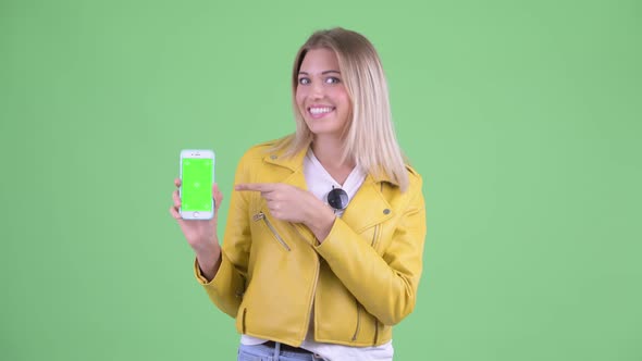 Happy Young Rebellious Blonde Woman Showing Phone and Giving Thumbs Up