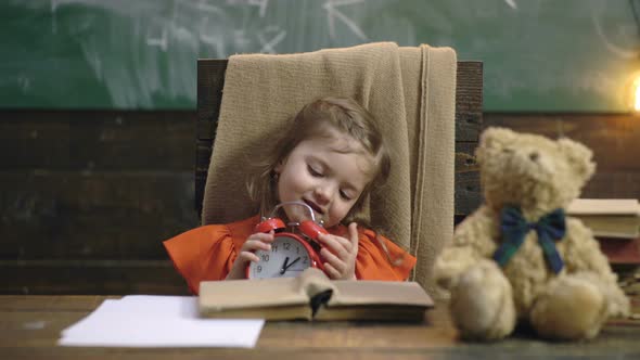 Cute Pupil in Classroom at Preschool. Little Girl Sitting at Desk and Playing with Alarm Clock