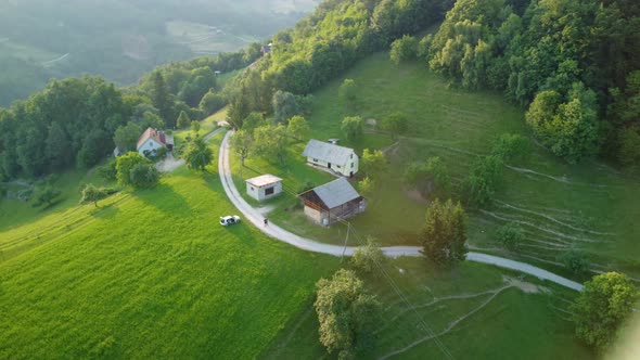 Flying around an idyllic small farm on top of the hill surrounded with green meadows and forest. Aer