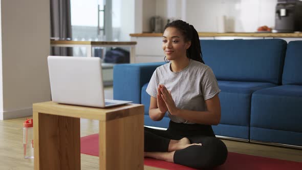 Young African Woman Doing Yoga Sitting in Front the Laptop