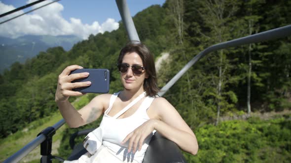 Beautiful Brunette Girl Makes Selfie and Sitting on Funicular or Cable-railway in Mountains in