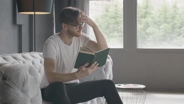 Handsome Man Adjusting Hair As Reading Book Indoors. Portrait of Brunette Young Caucasian Reader