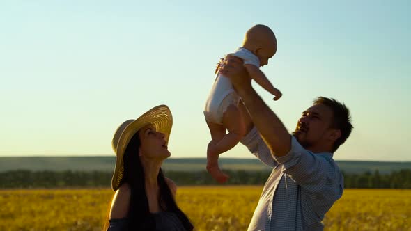 Loving parents playing with baby in wheat field in summer