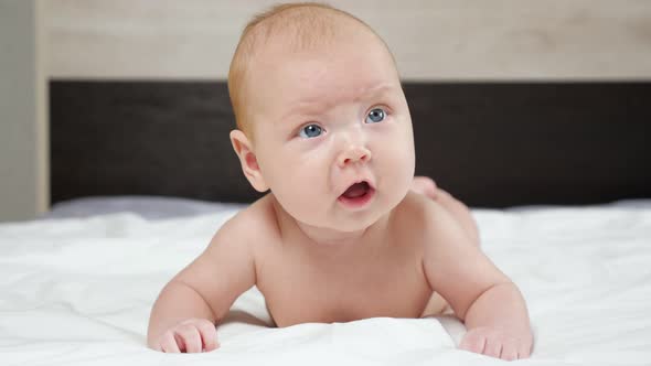 Cute Baby Girl Frowns Trying to Raise Up Head Lying on Bed