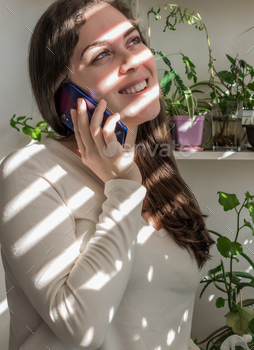 Young Caucasian woman making a phone call with a smart phone on her balcony on a sunny day
