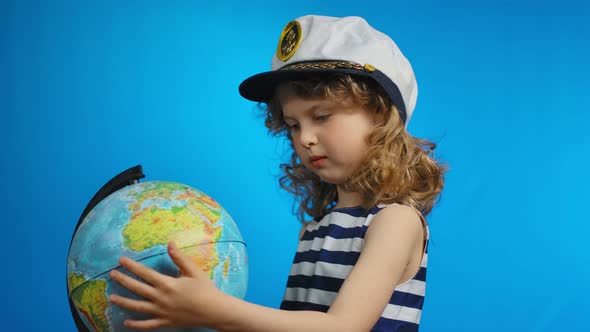 Little Curly Blond Girl in Sailor Hat is Pointing Her Finger Into the Globe