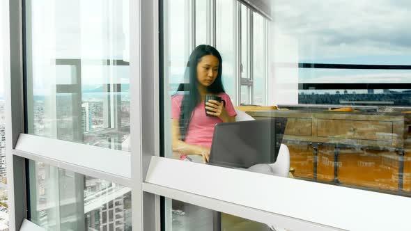 Woman using laptop while having cup of coffee